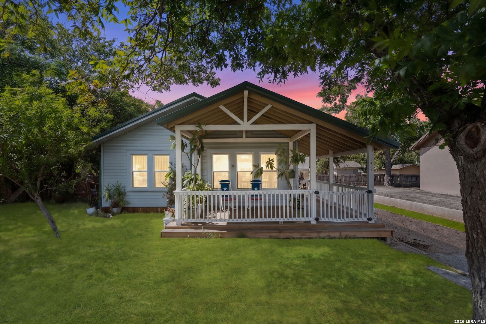 Blue house with a wide covered porch and white railings beneath mature trees at dusk.