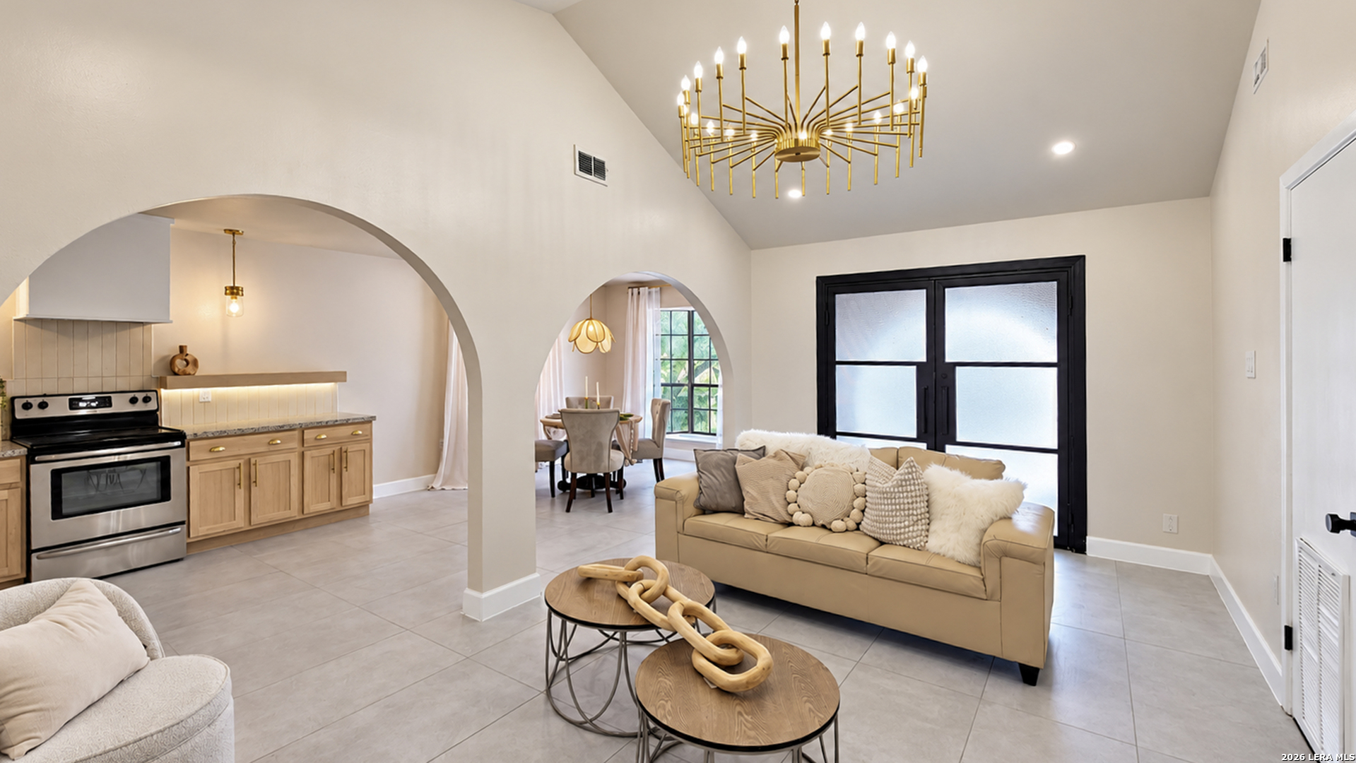 Open-concept living room with arched kitchen and dining openings and a sculptural gold chandelier.