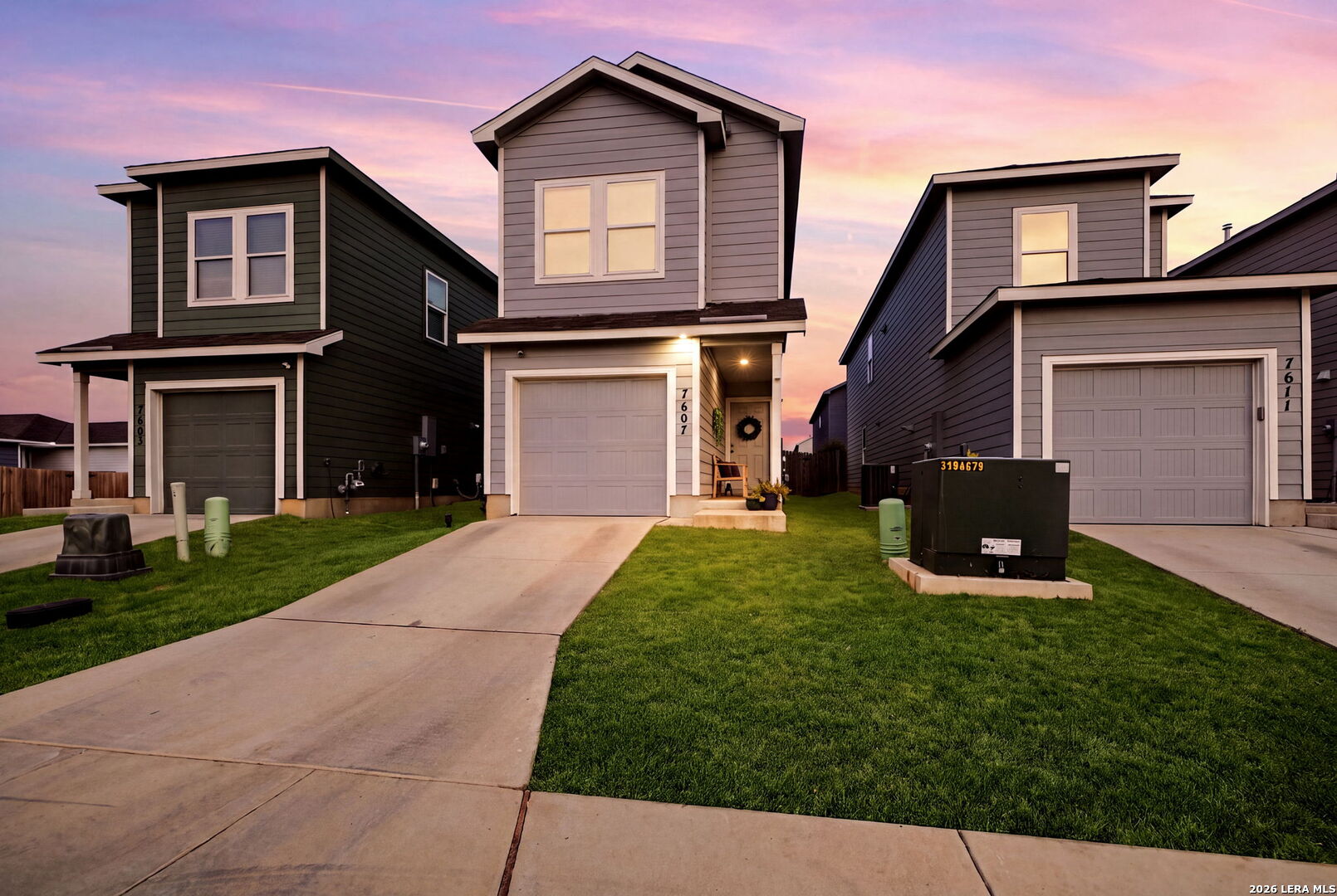Two-story gray home with a front-facing garage and covered entry at sunset.