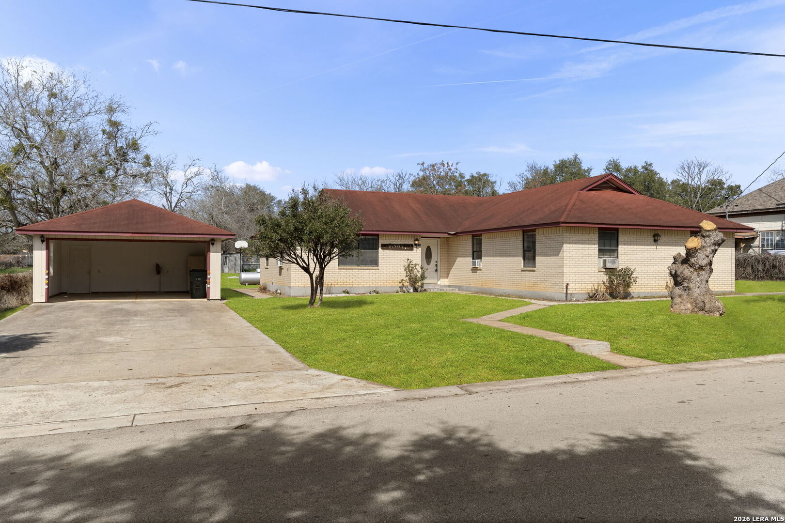 Single-story brick house with a red roof, detached garage, and green front lawn.
