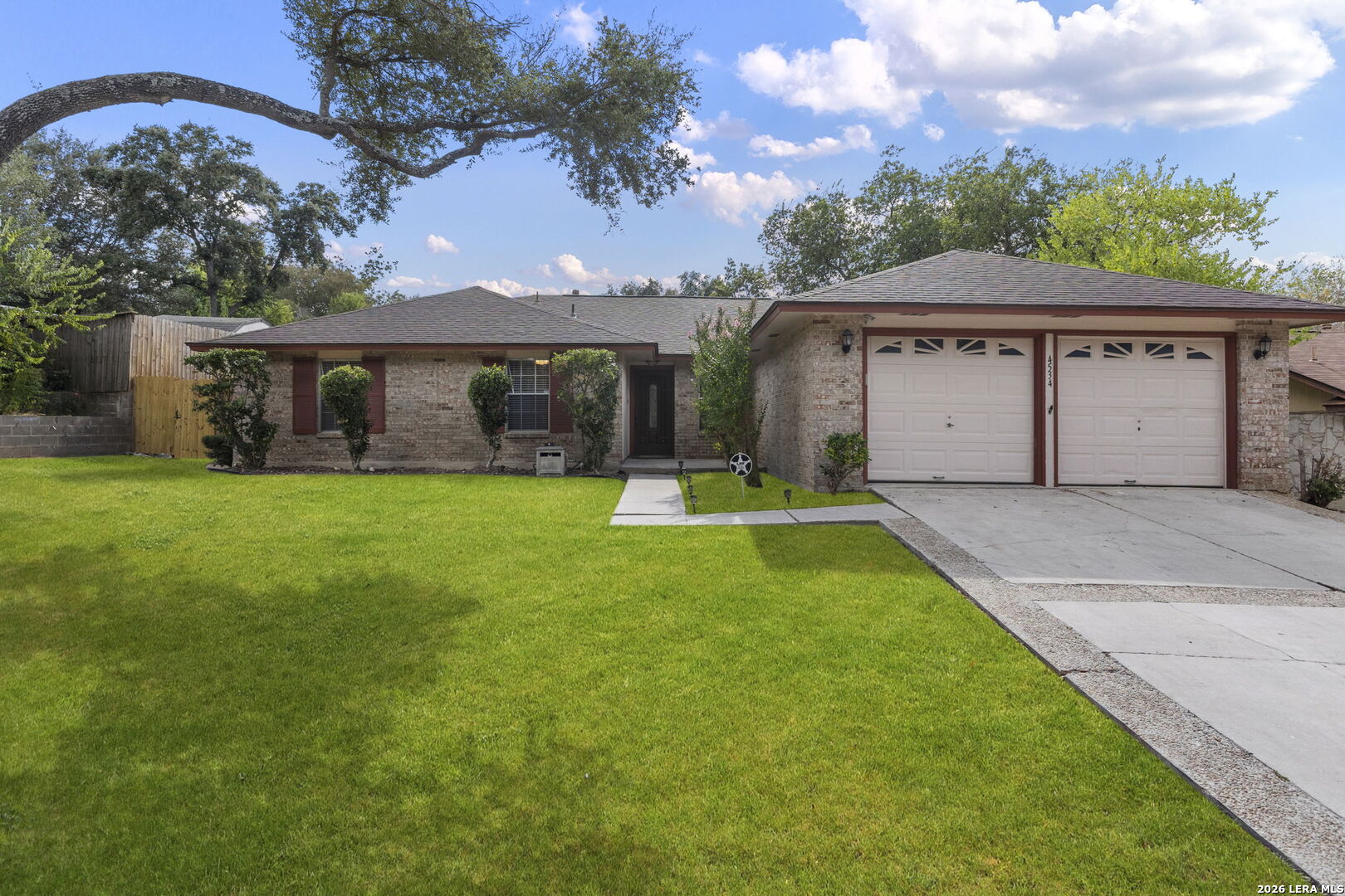 Single-story brick home with a two-car garage, broad lawn, and mature shade trees.