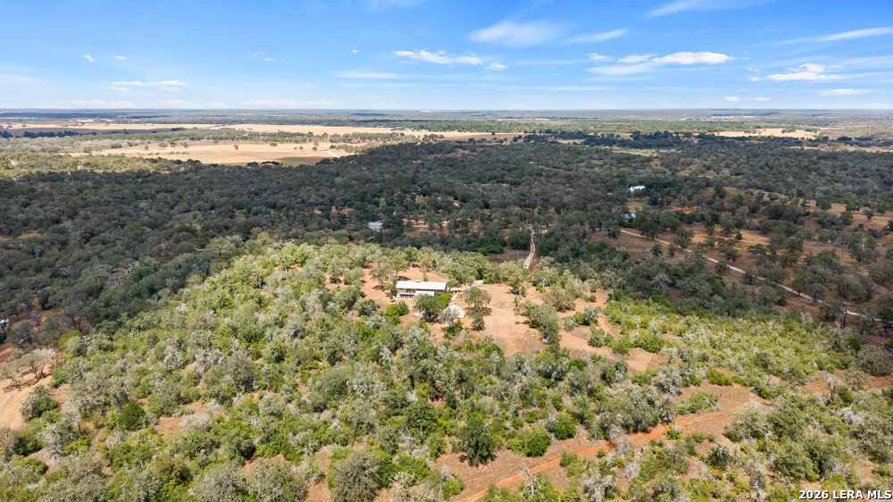 Aerial view of a home nestled among trees, with open fields and wooded land extending to the horizon.