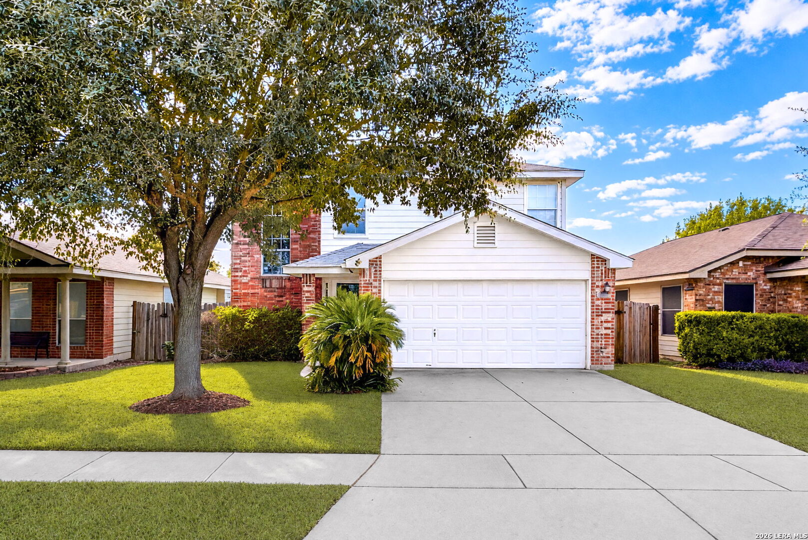 Two-story brick-and-white suburban home with a double garage, broad driveway, and large shade tree.