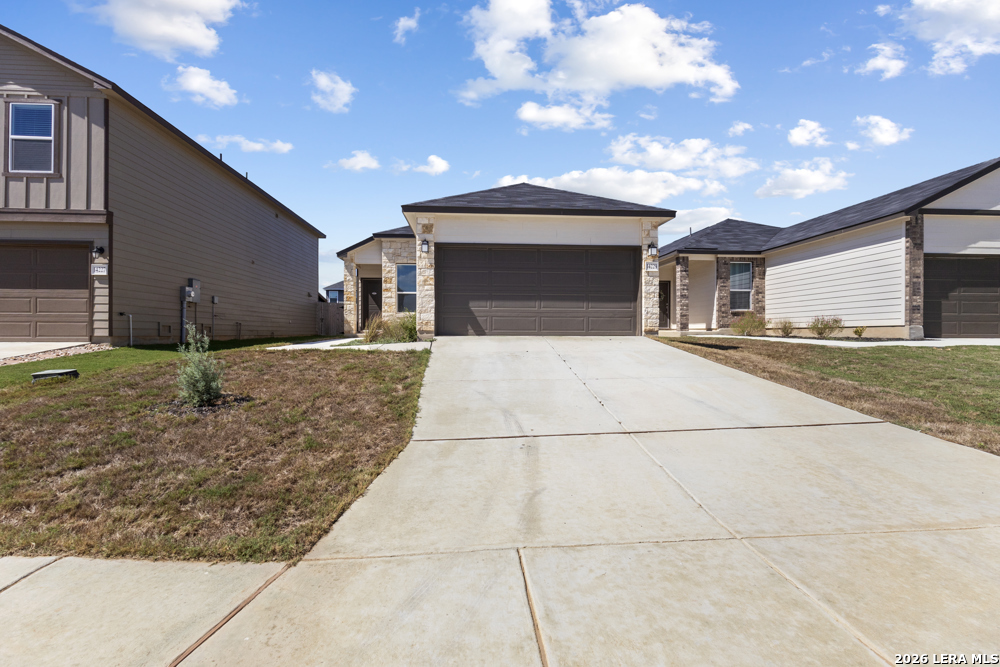 Single-story home with stone accents, a dark double garage door, and a wide concrete driveway.