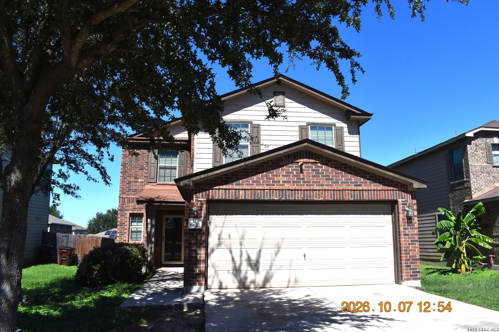 Two-story brick-and-siding house with a wide attached garage beneath a mature shade tree.
