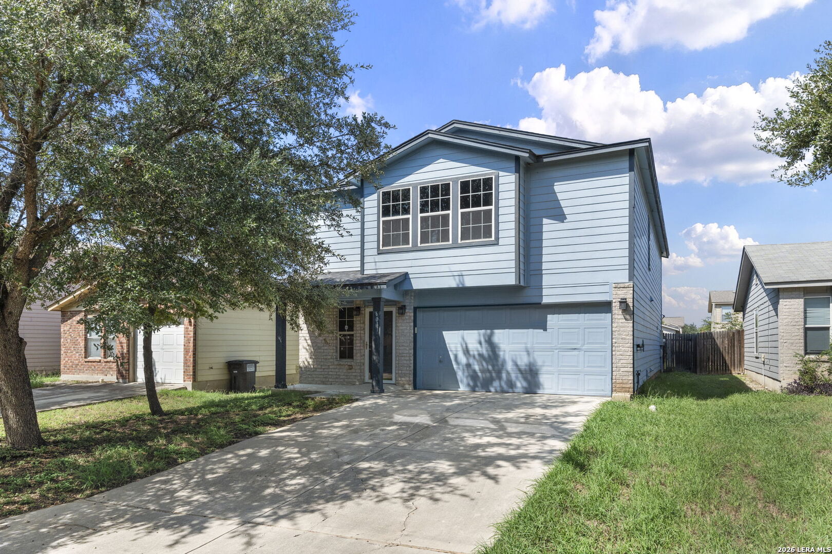 Two-story blue house with a double garage, shaded by mature trees.