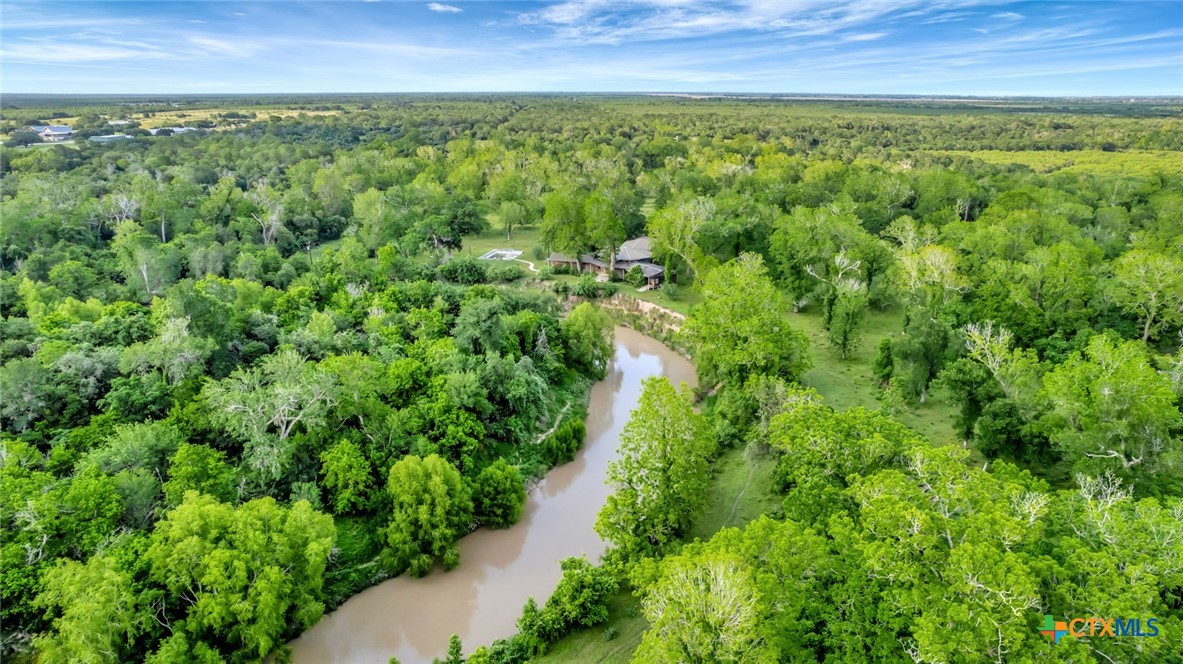 Aerial view of a wooded ranch with a winding river, open pasture, and a swimming pool.
