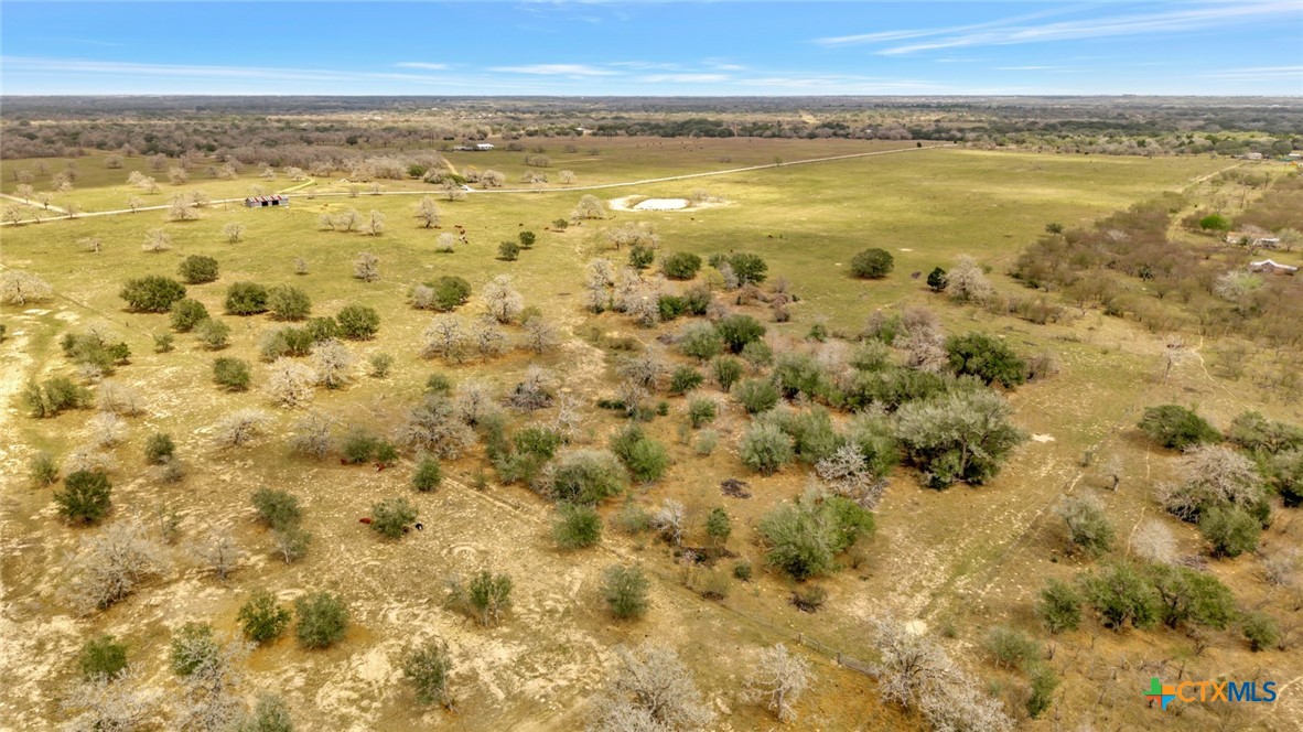 Aerial view of open ranchland with scattered trees, a small pond, and distant road.