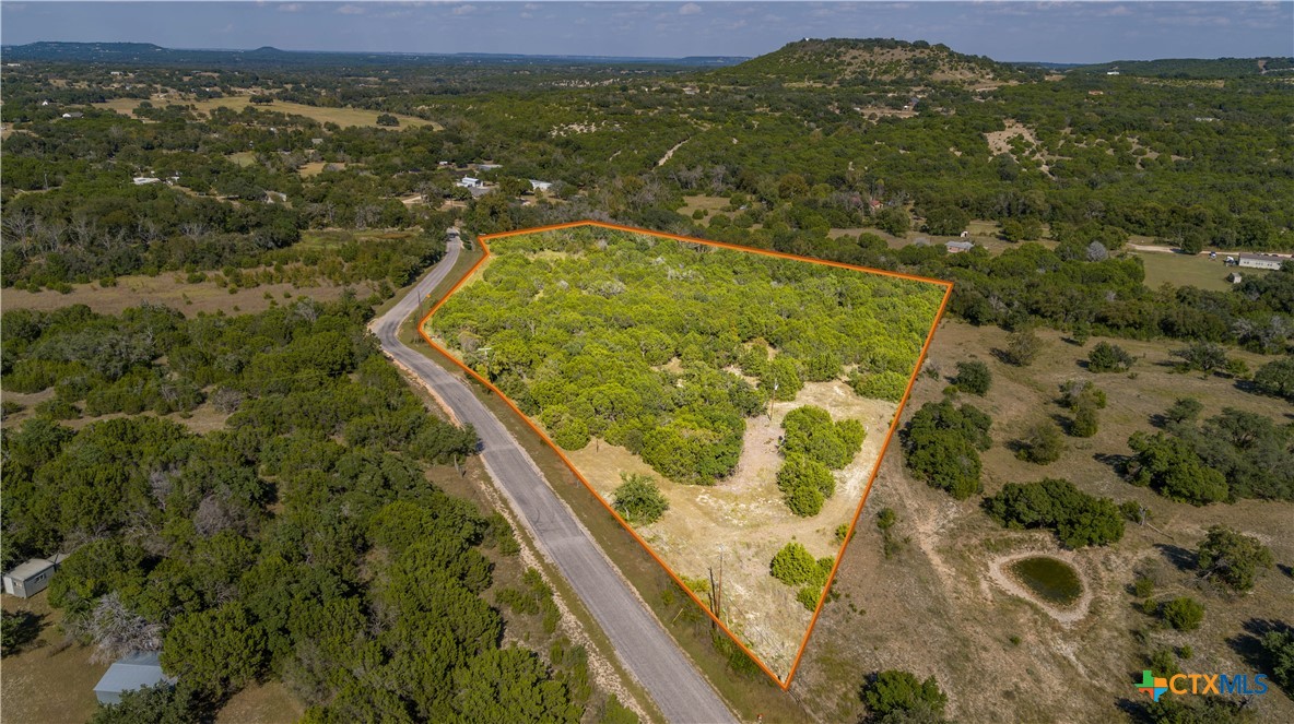 Aerial view of a wooded vacant lot outlined in orange beside a rural road.