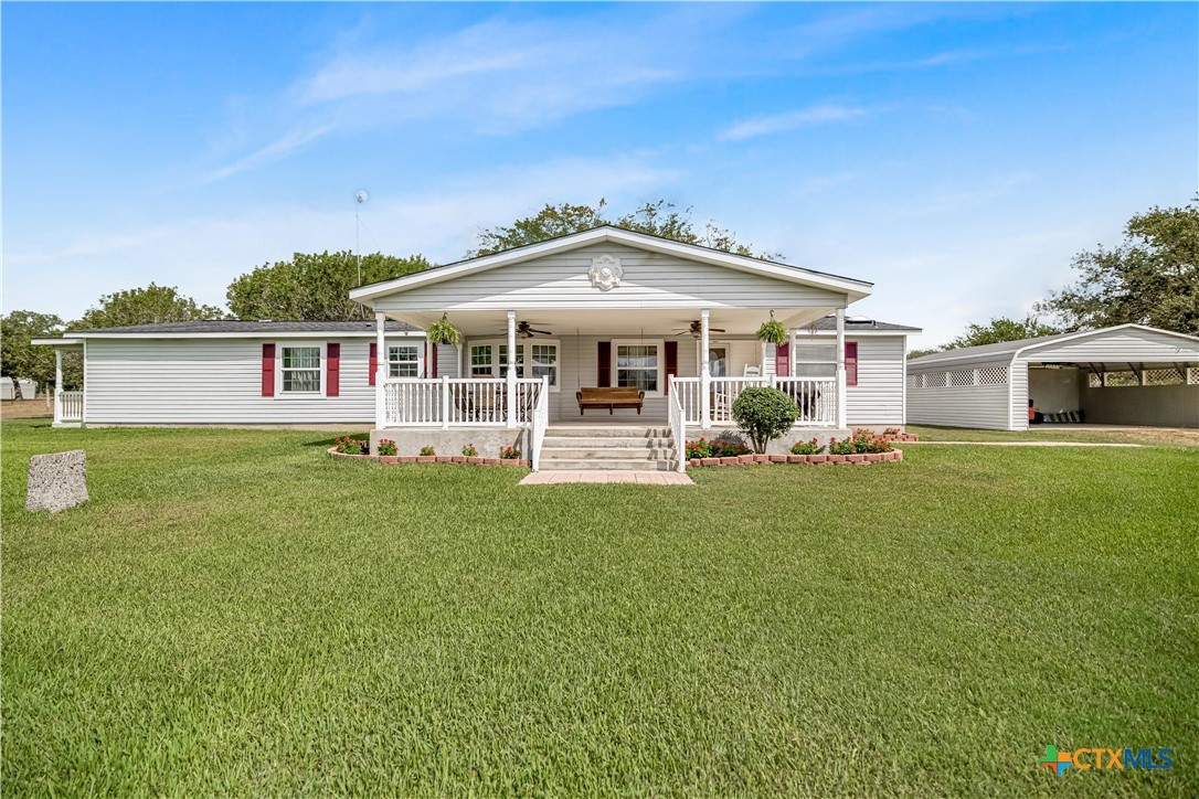 Single-story ranch home with red shutters, a broad lawn, covered porch, and detached carport.