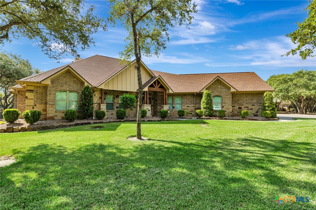 Single-story stone and brick home with a covered entry, broad green lawn, and mature trees.