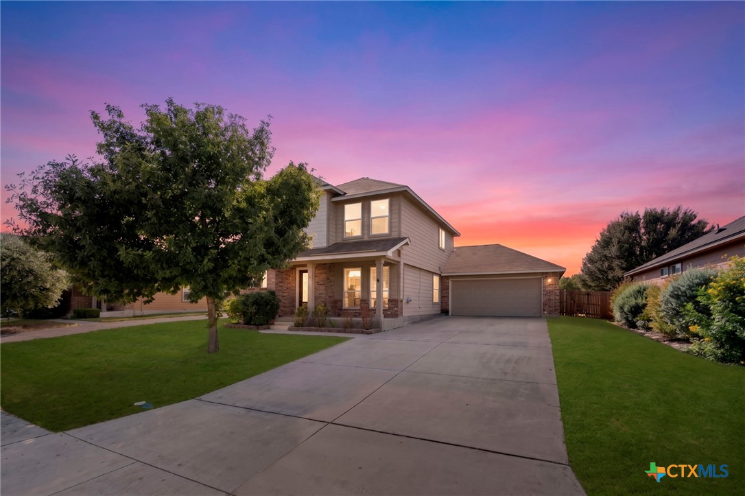 Two-story house with an attached garage and wide driveway beneath a vivid sunset sky.