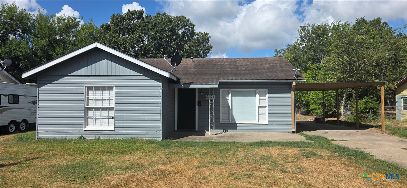 Gray single-story house with white-trimmed windows and a wooden carport beside the driveway.
