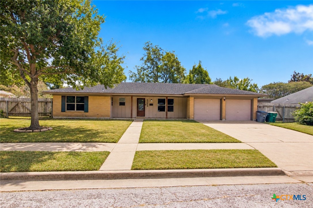 Single-story brick home with an attached two-car garage, broad front lawn, and large shade tree.