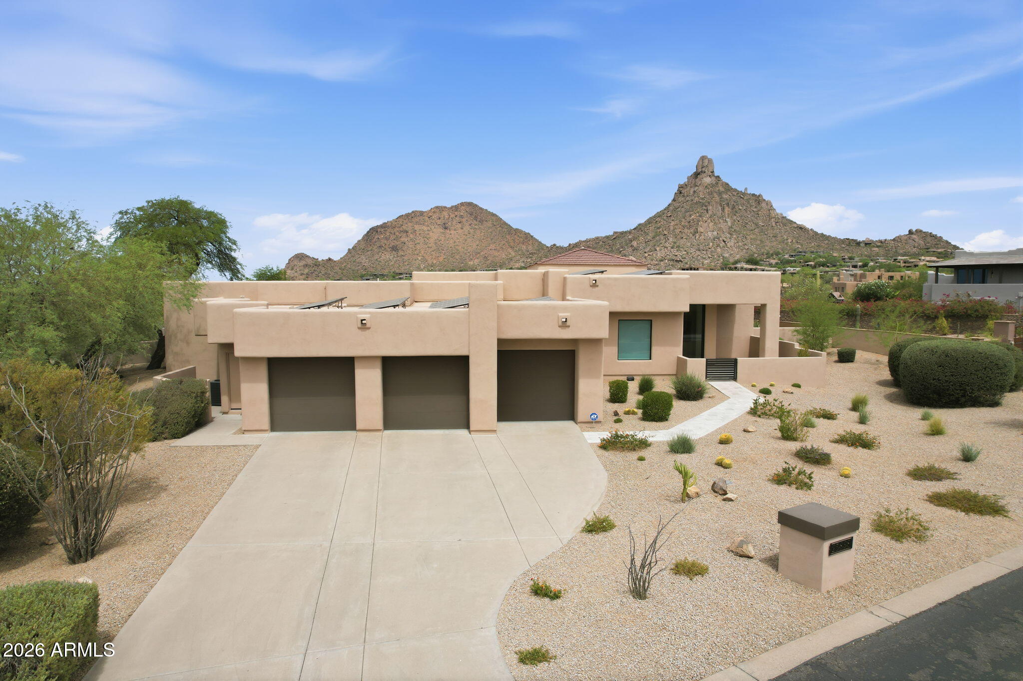 Contemporary stucco home with a three-car garage, desert landscaping, and rugged mountains behind it.