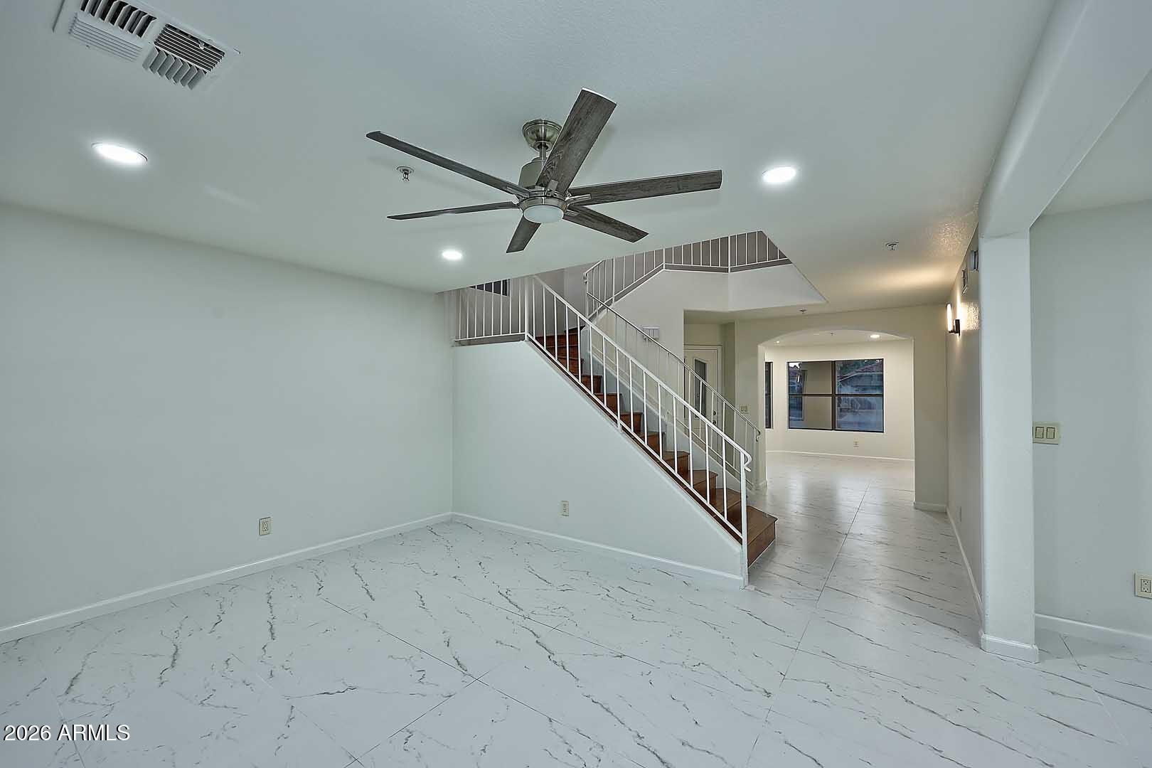 Vacant living area with marble-look tile flooring and a staircase with white railings and wood treads.