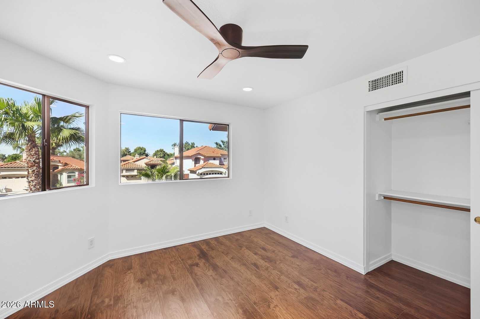 Vacant bedroom with wood-look flooring, a ceiling fan, two windows, and an open closet.