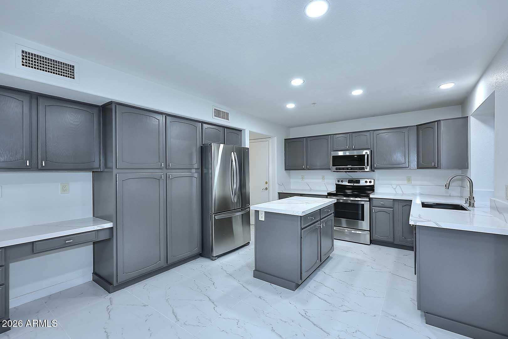 Kitchen with gray cabinetry, white stone-look counters, a center island, and stainless steel appliances.