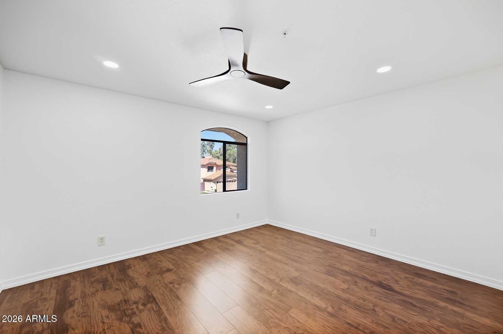 Vacant bedroom with wood-look flooring, a ceiling fan, and an arched window.