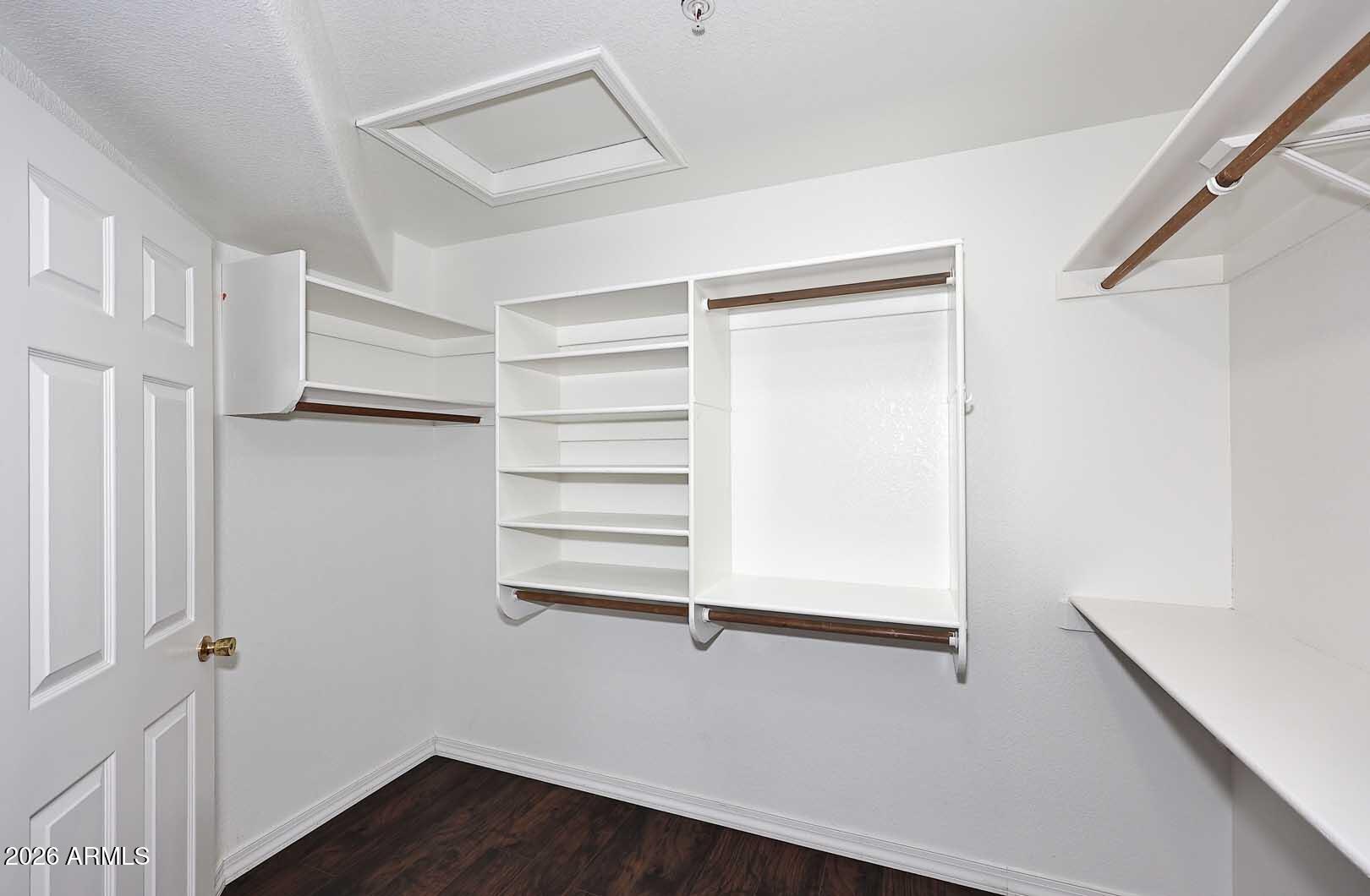 Walk-in closet with white built-in shelving and hanging rods, plus dark wood flooring.
