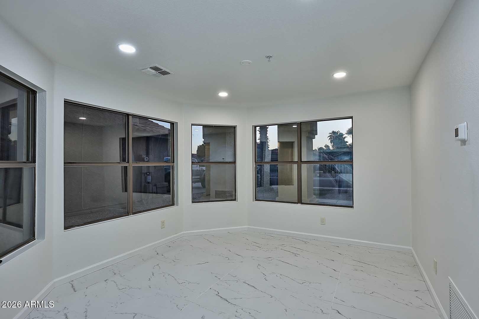 Vacant room with large windows, marble-look tile flooring, and recessed lights.