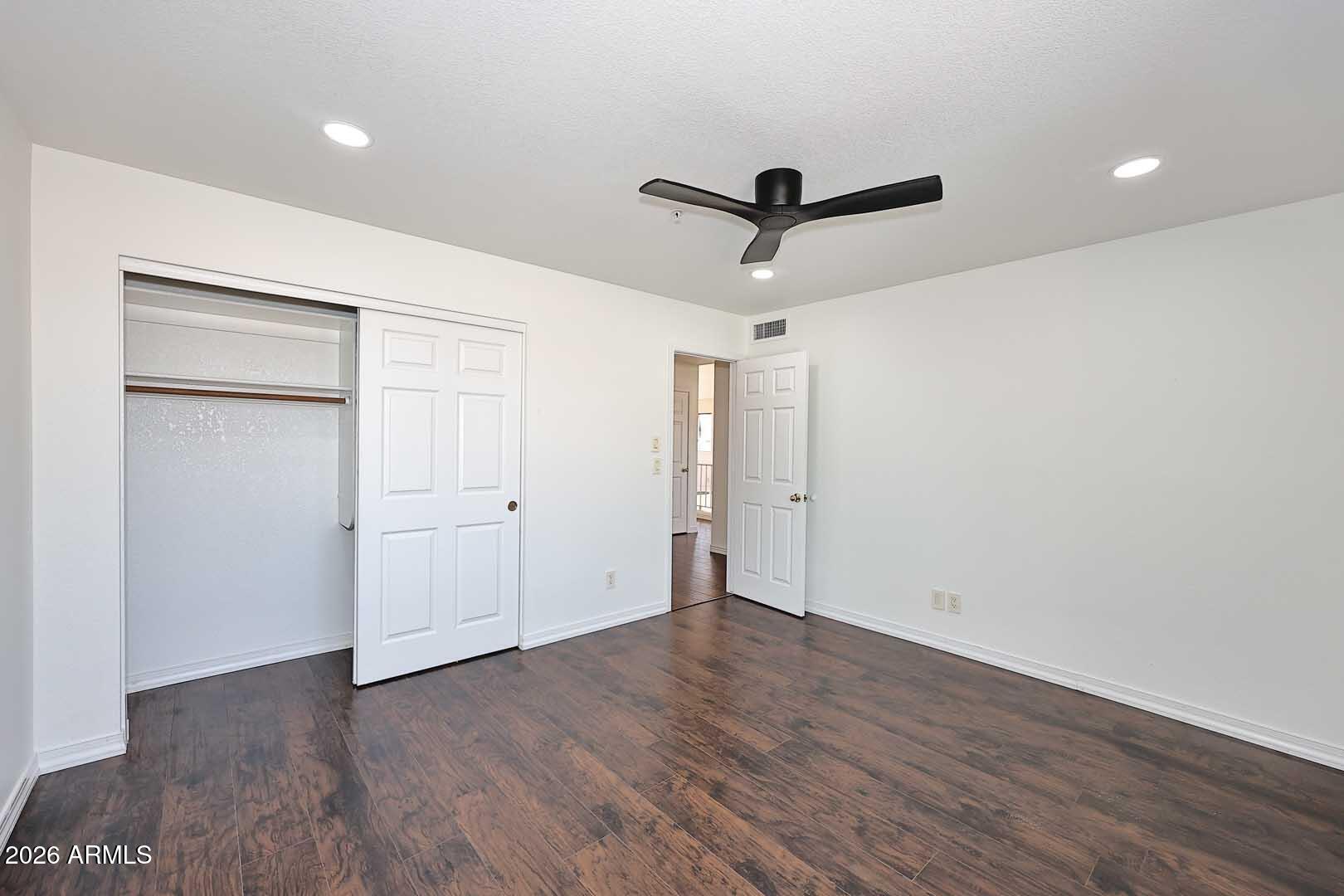 Vacant bedroom with dark wood-look flooring, a black ceiling fan, and a partly open closet.