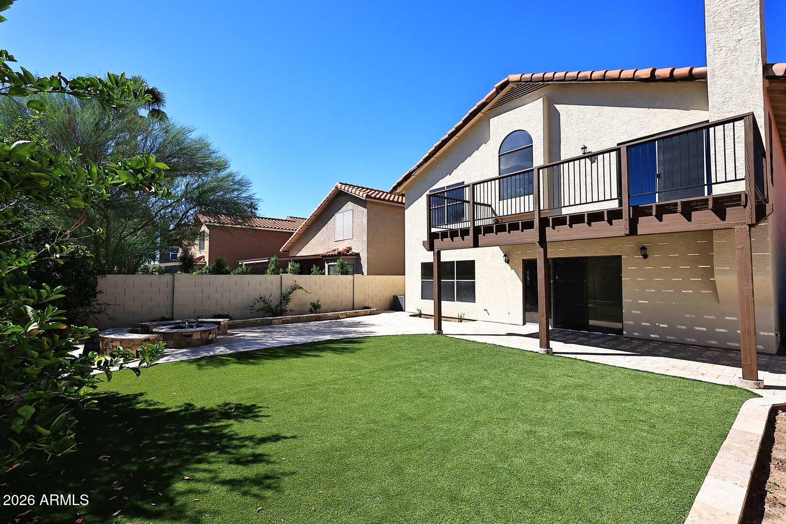 Backyard with a broad lawn, circular stone fire pit, and two-story home with a wooden balcony.