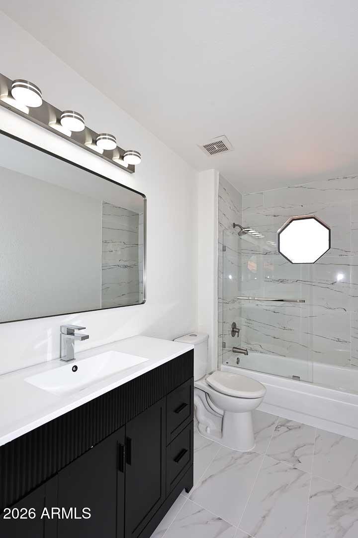 Bathroom with a black fluted vanity and marble-look tile around the tub and shower.