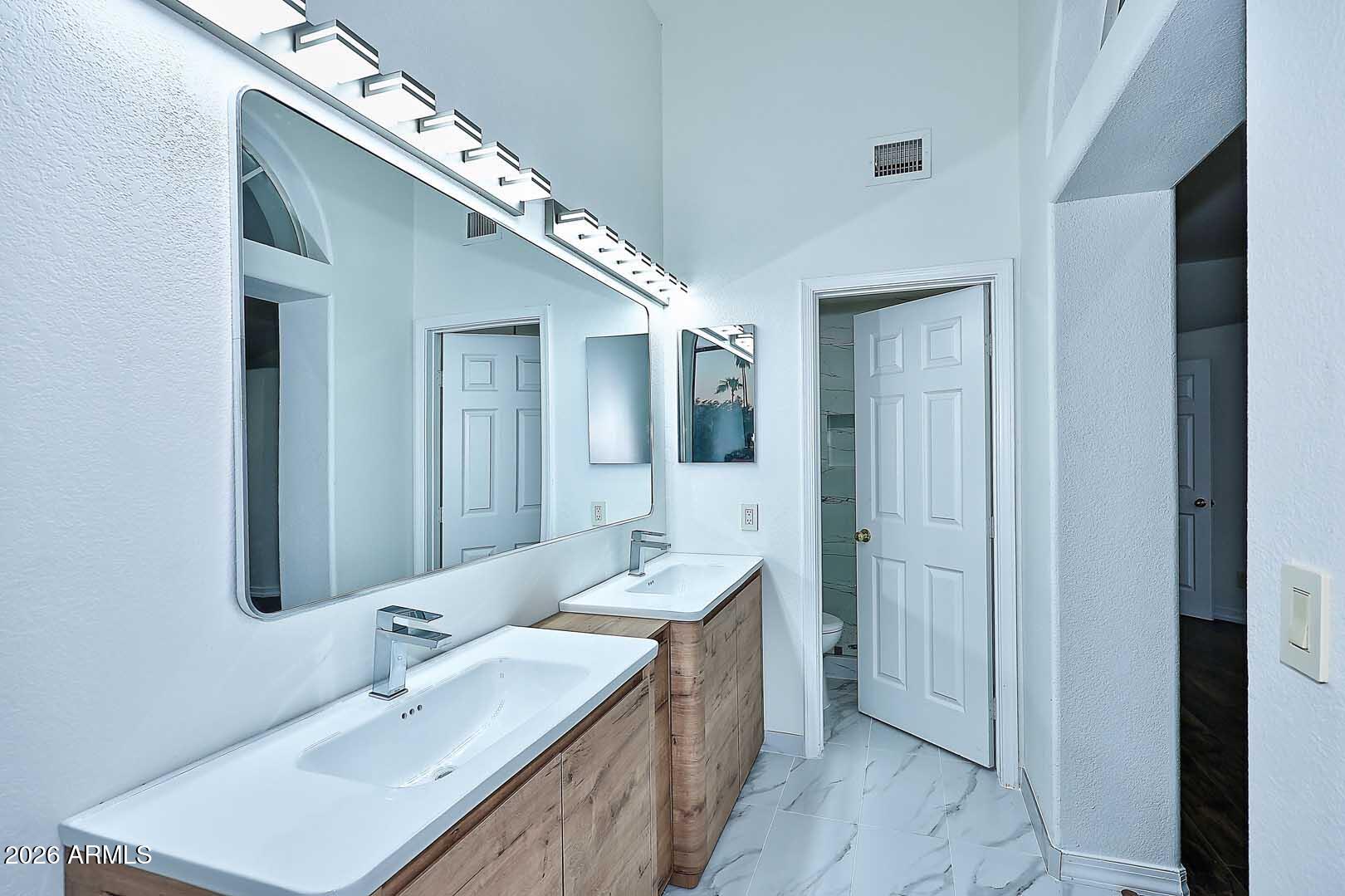 Bathroom with a double-sink wood vanity, large mirror, and marble-look tile floor.