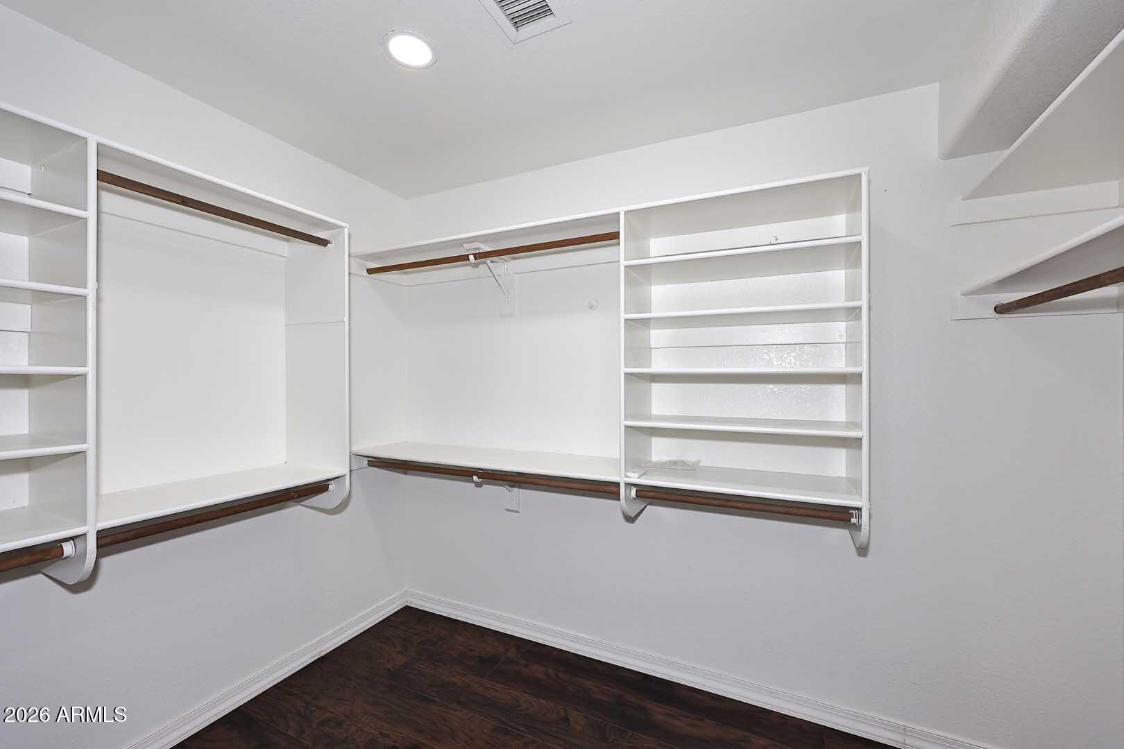Walk-in closet with built-in white shelving, hanging rods, and dark wood flooring.