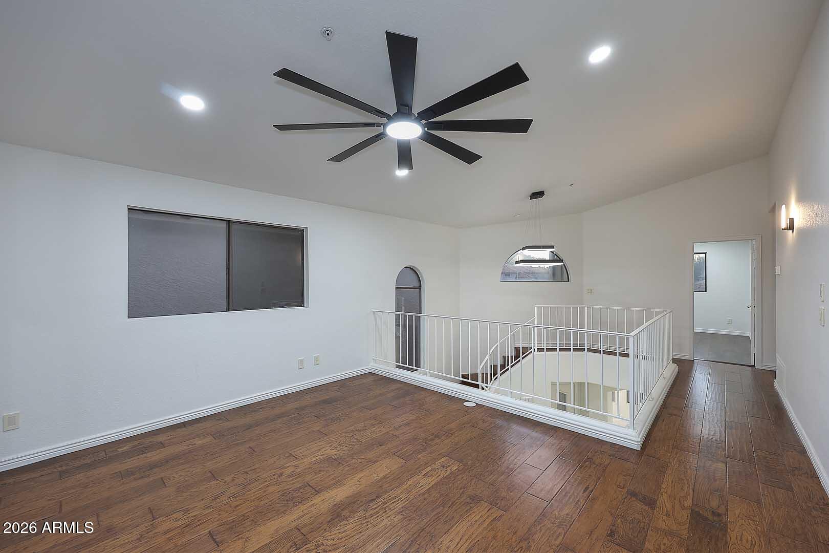 Upstairs landing with dark wood floors, a large ceiling fan, and white railing around an open stairwell.