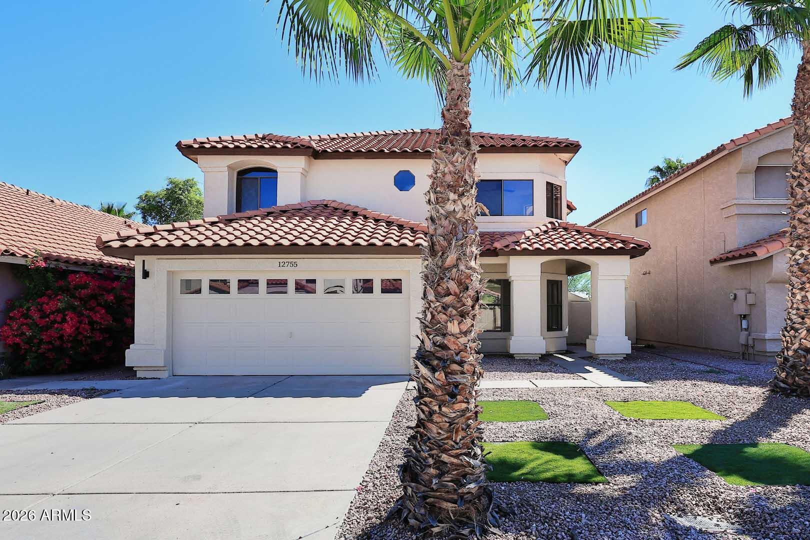 Two-story stucco home with a red tile roof, palm trees, and desert landscaping.