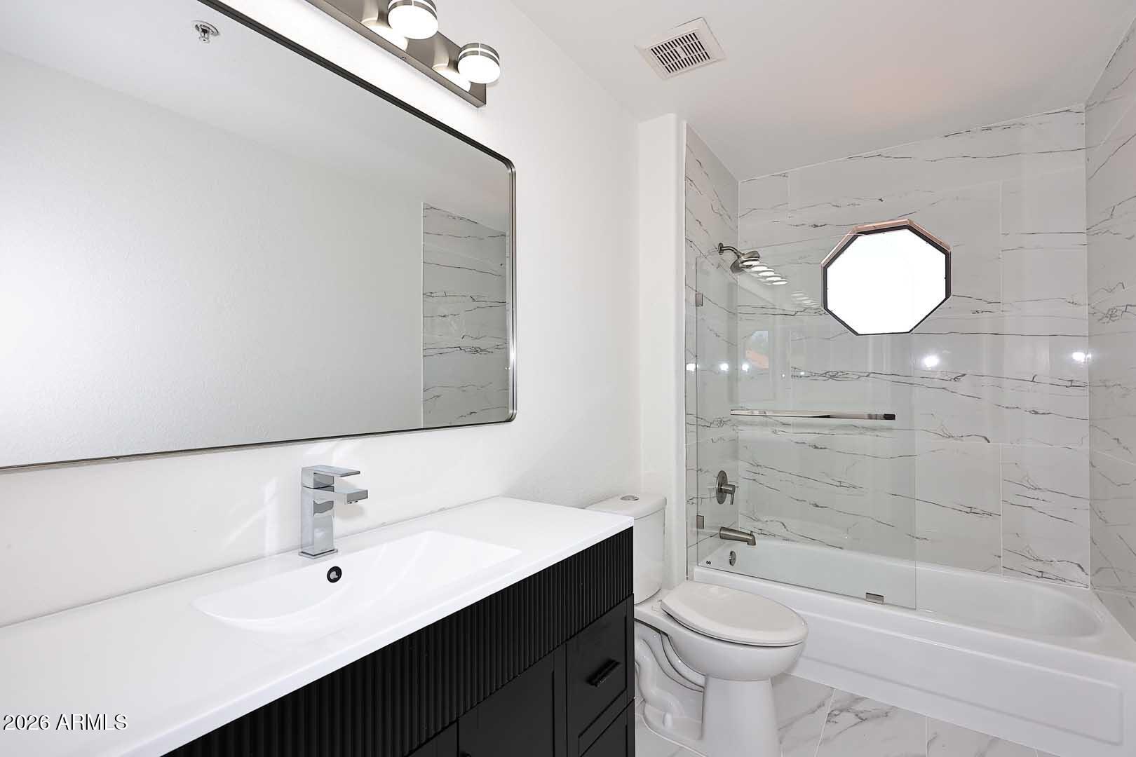 Modern bathroom with a black fluted vanity and glass-enclosed tub-shower lined with marble-look tile.