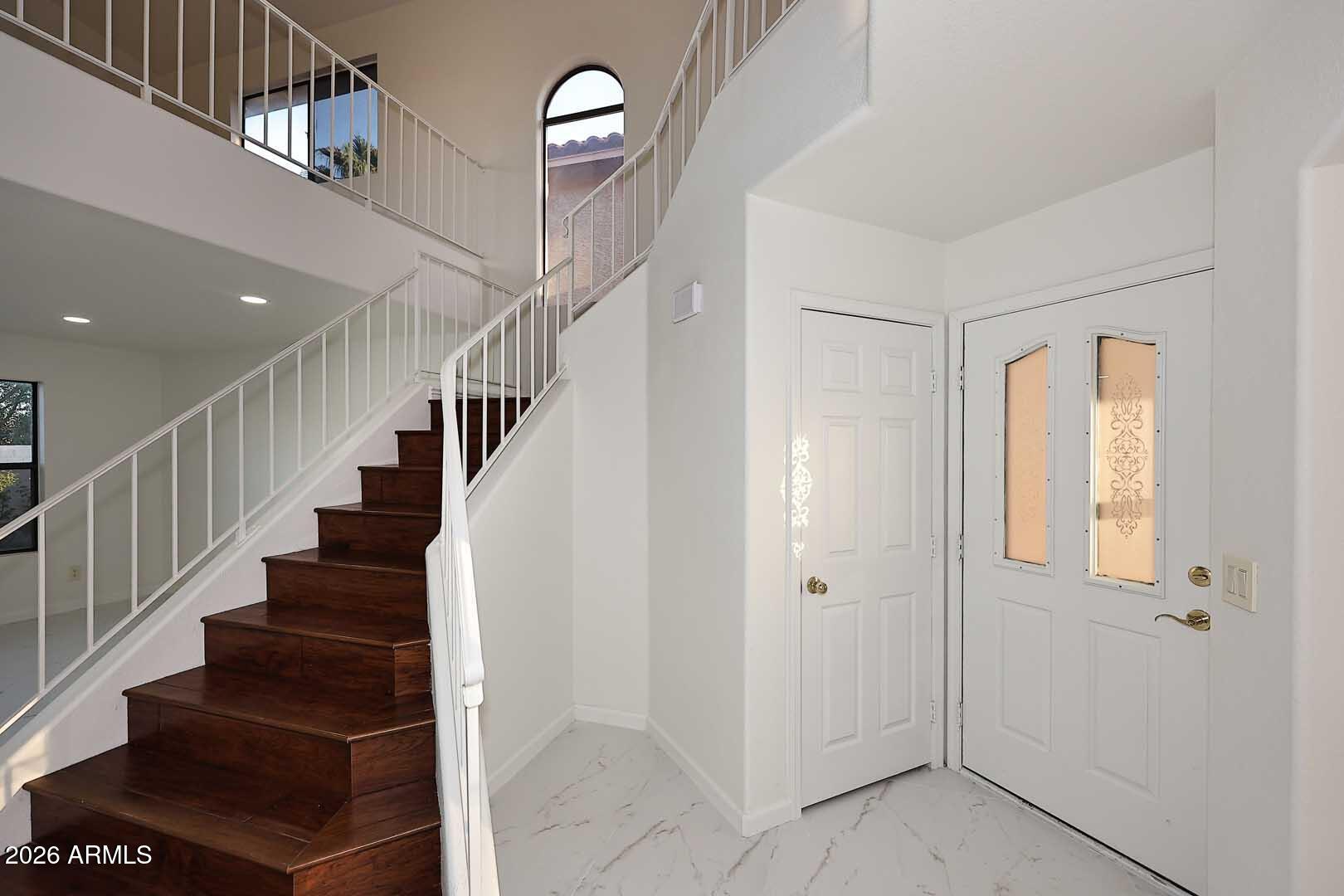 Entry foyer with a dark wood staircase, white front door with decorative glass, and marble-look tile floor.