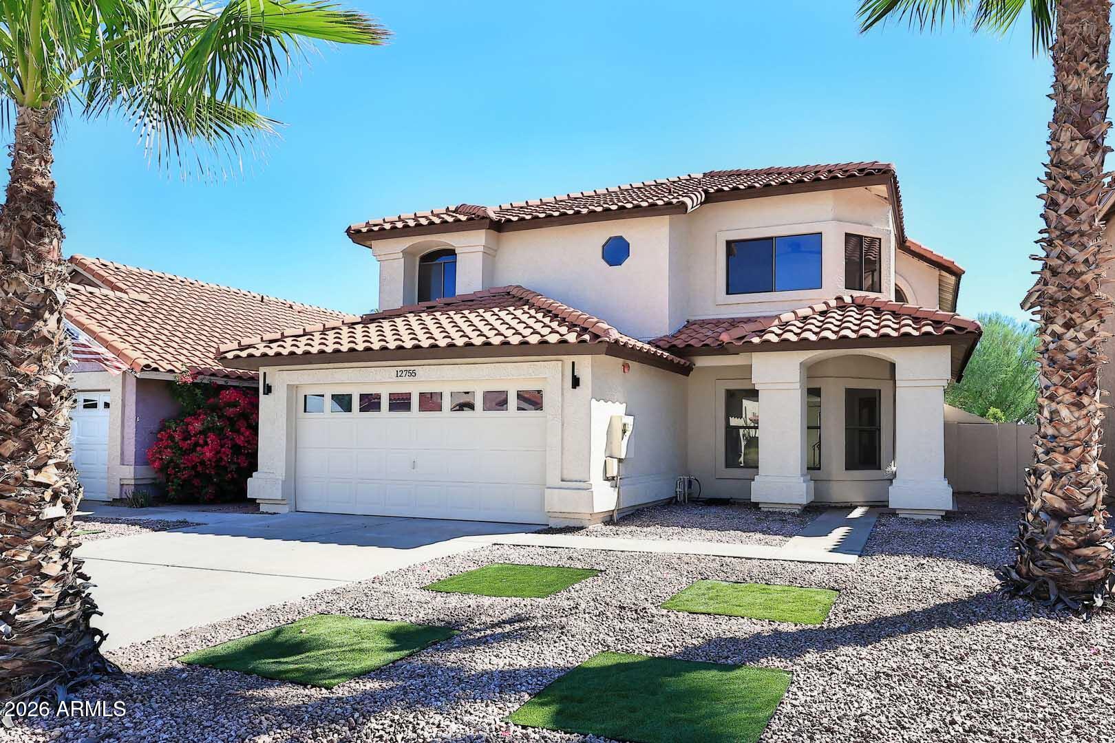 Two-story stucco home with a tile roof, two-car garage, palm trees, and gravel landscaping.