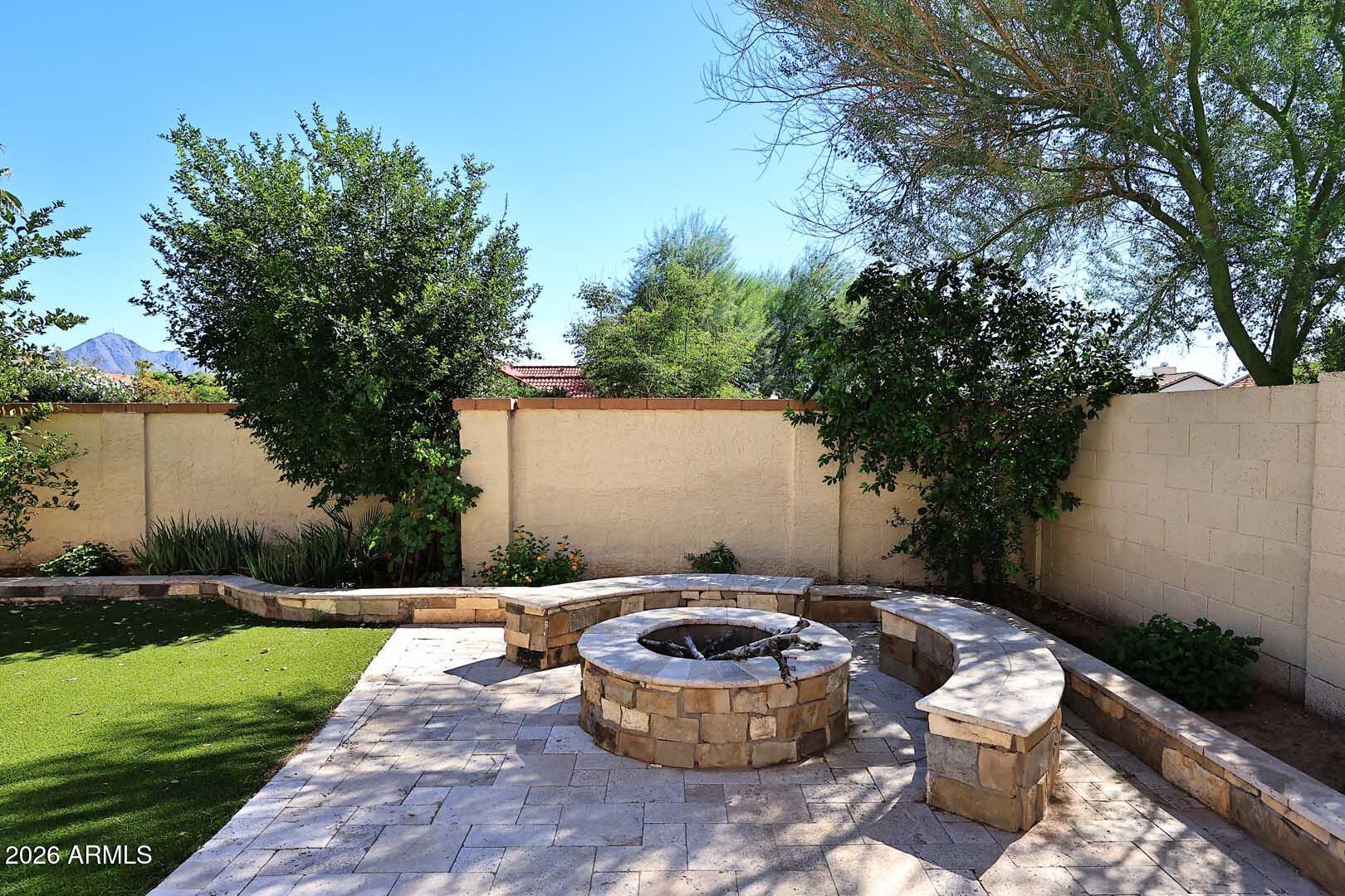 Backyard patio with a circular stone fire pit, curved built-in benches, and a mountain view.