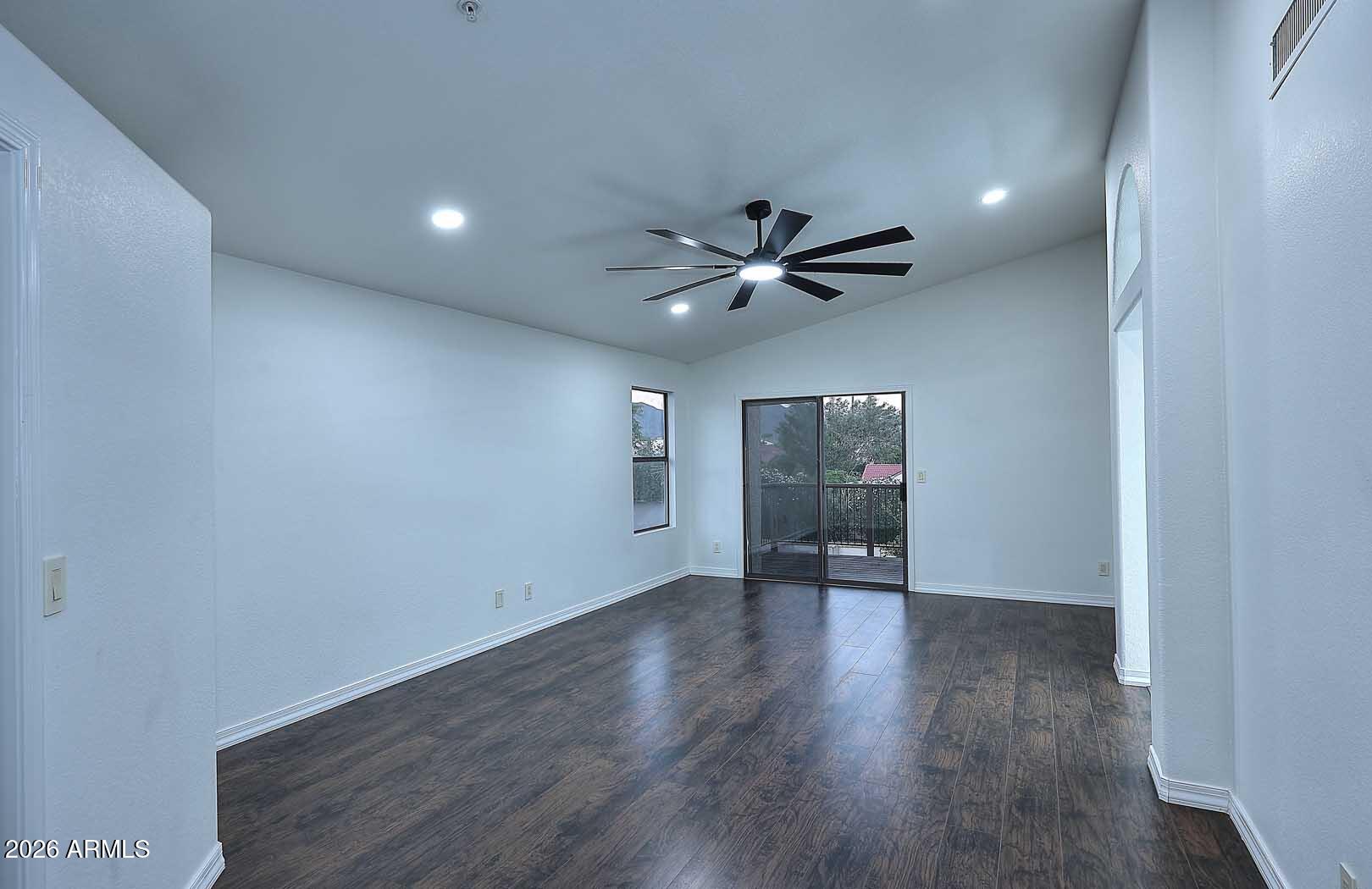 Empty room with dark flooring, a large ceiling fan, and sliding glass doors to a balcony.