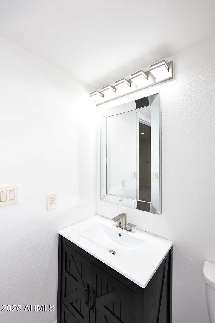 Bathroom vanity with a white sink, dark paneled cabinet, rectangular mirror, and modern light.