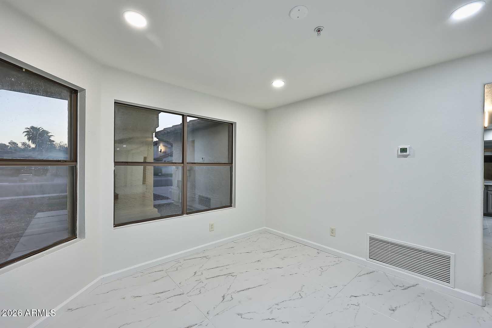 Vacant room with marble-look tile flooring, large windows, and recessed lights.