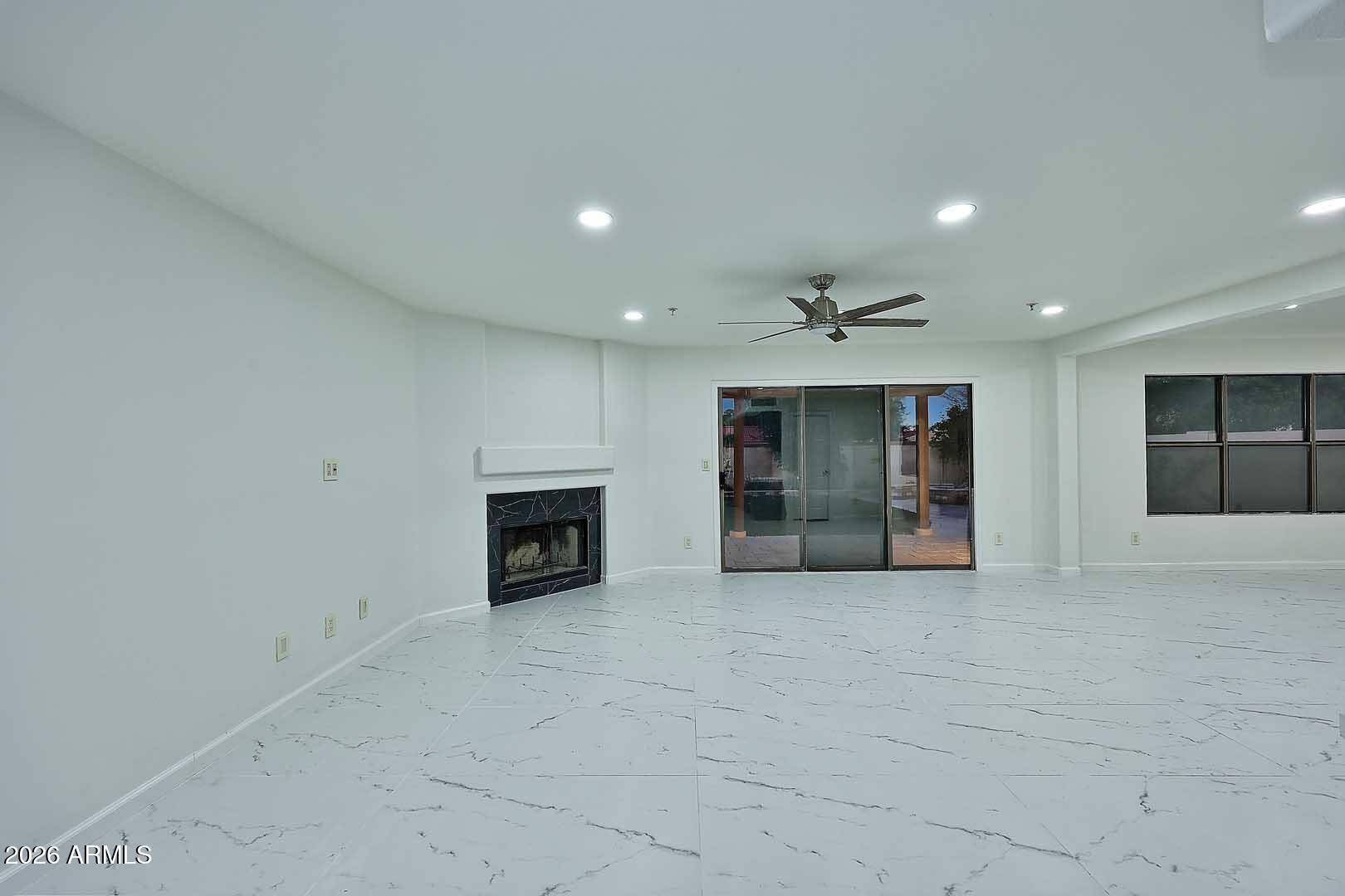 Vacant living room with a dark-tiled fireplace, marble-look floors, and sliding glass doors to a patio.