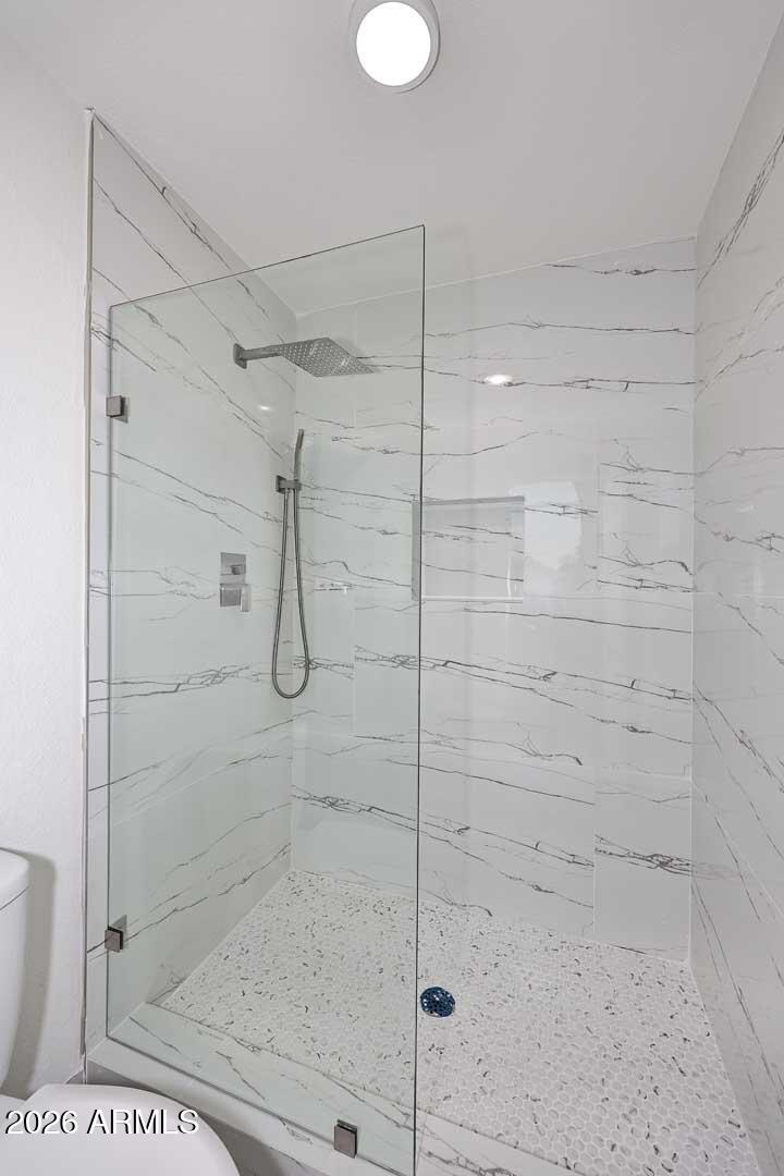 Walk-in shower with glass panels, marble-look tile, rainfall showerhead, and pebble floor.