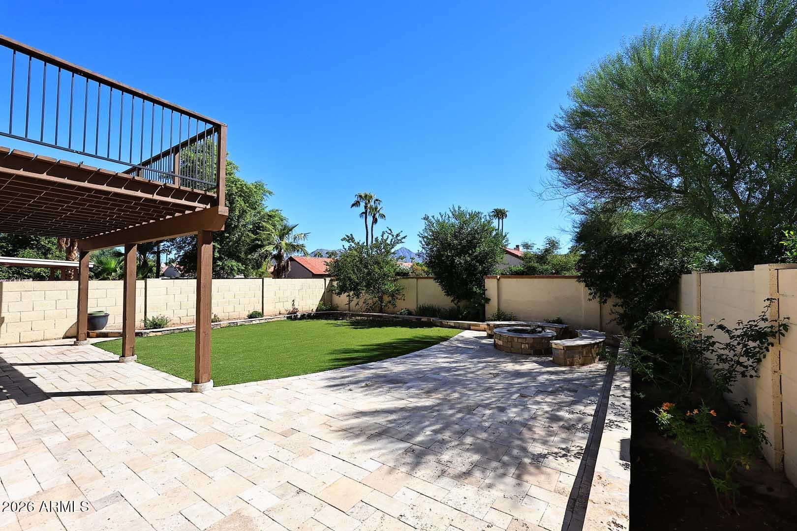 Backyard patio with artificial turf, a raised deck, and a circular stone fire pit.