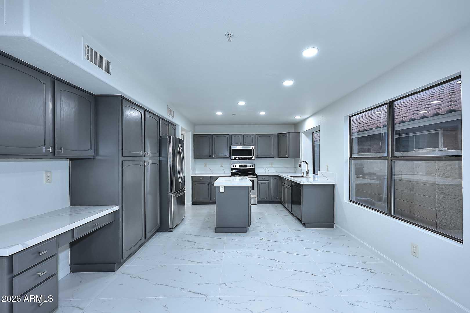Vacant kitchen with dark gray cabinets, white marble-look surfaces, a center island, and large windows.