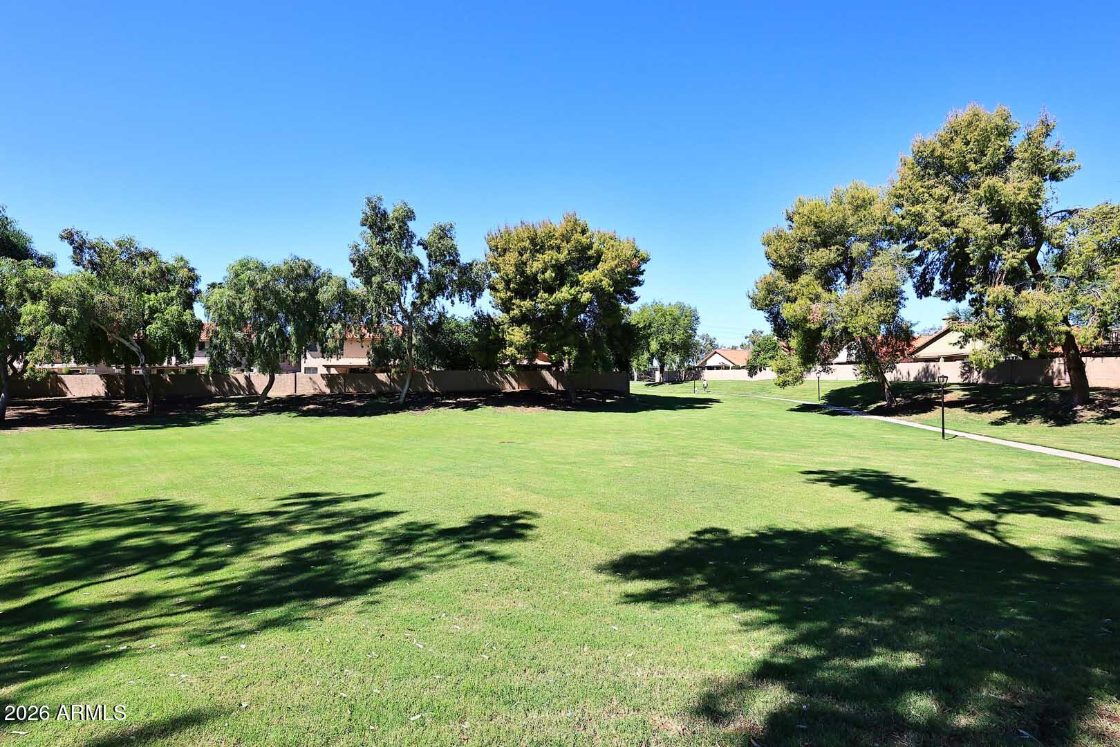 Neighborhood greenbelt with a broad lawn, mature trees, and a paved walkway.