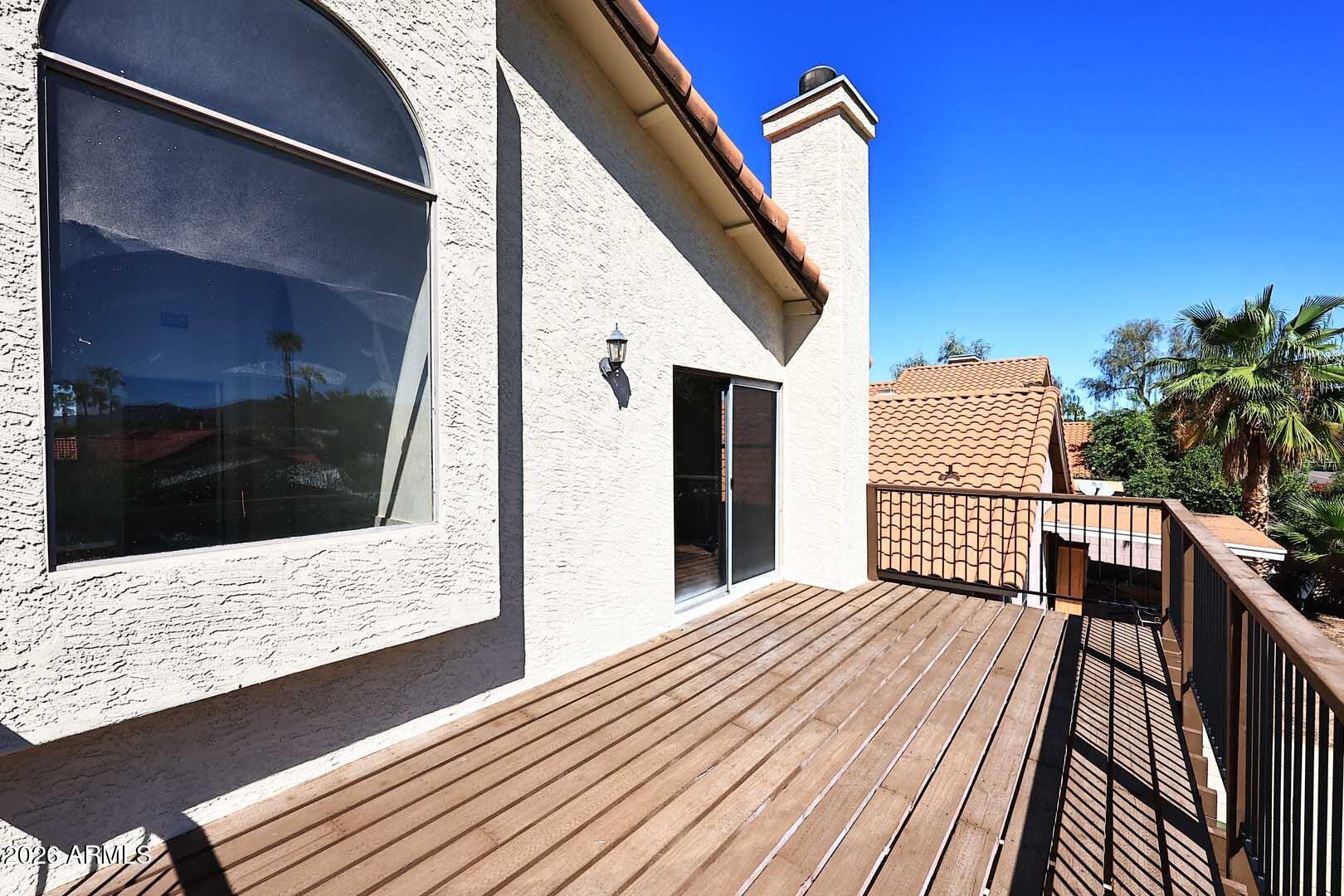 Wooden deck beside a stucco house, with metal railings and palm trees beyond.