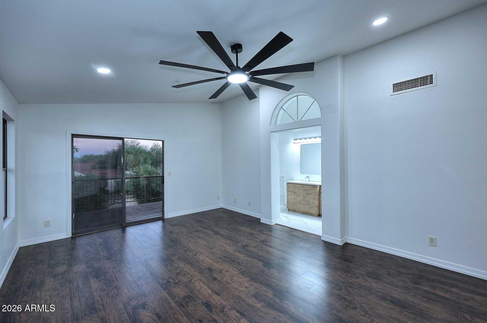 Empty bedroom with dark flooring, a large ceiling fan, and sliding glass doors to a balcony.