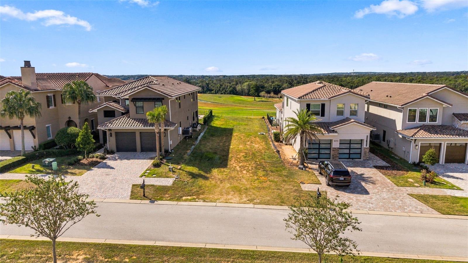 Aerial view of Clermont homes flanking a vacant grassy lot, with wooded land beyond.