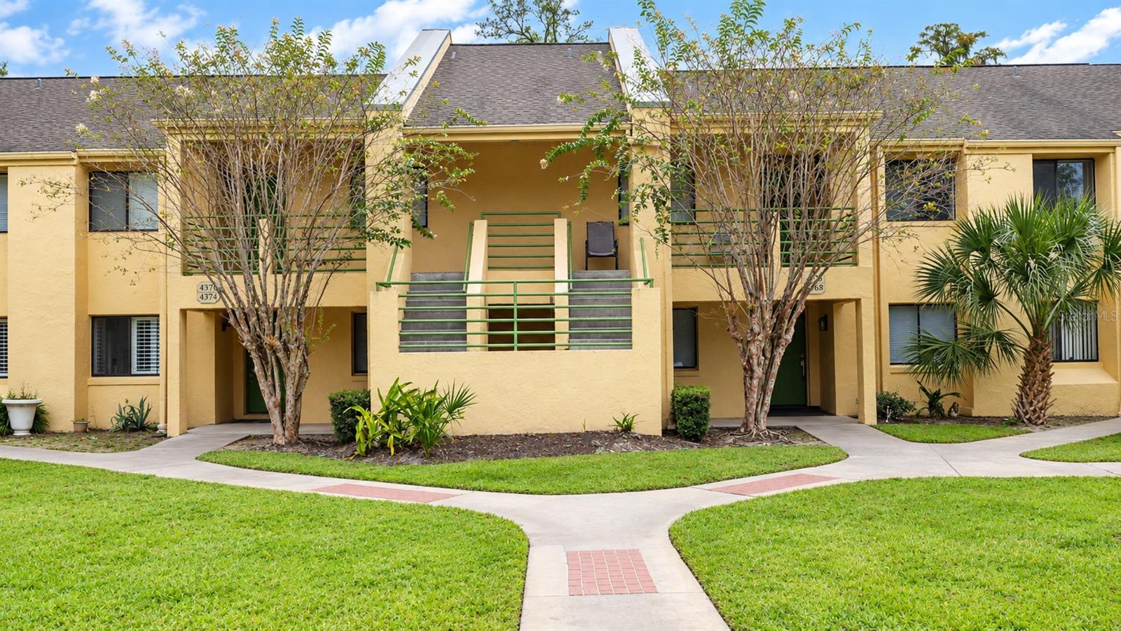 Yellow two-story condominium building with a central staircase and landscaped lawn.