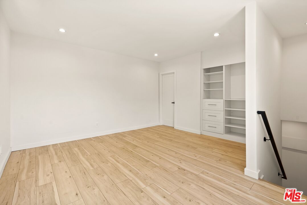 Empty room with light wood floors, recessed lights, and built-in shelving