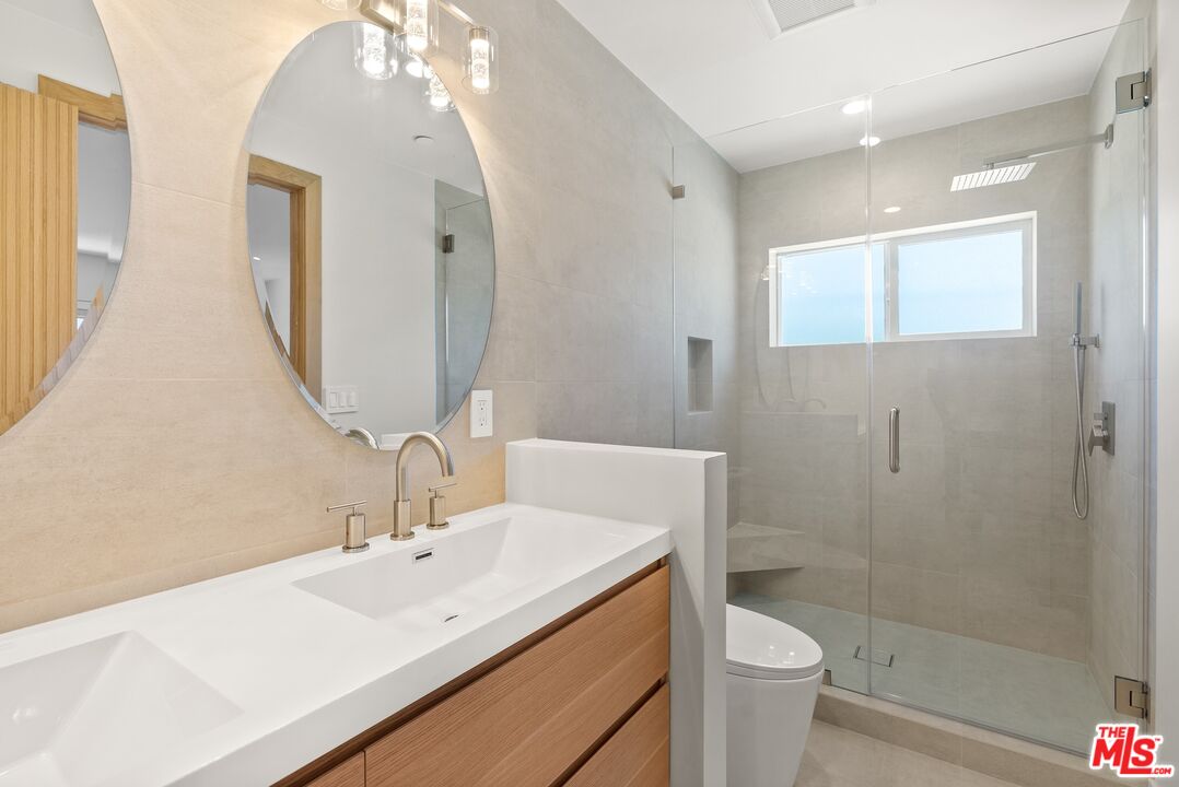 Modern bathroom with a wood-front vanity, oversized oval mirror, and glass-enclosed tiled shower.
